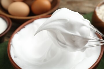Whipped egg whites in bowl, whisk and ingredients on table, closeup