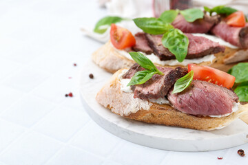 Delicious bruschettas with roast beef served on white tiled table, closeup. Space for text