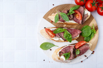 Delicious bruschettas with roast beef served on white tiled table, flat lay. Space for text