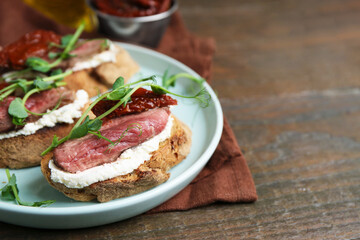 Delicious bruschettas with roast beef served on wooden table, closeup. Space for text