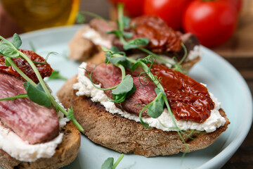 Delicious bruschettas with roast beef served on wooden table, closeup