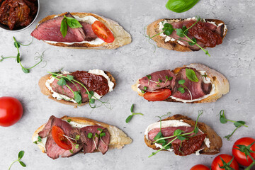 Delicious bruschettas with roast beef served on light table, flat lay