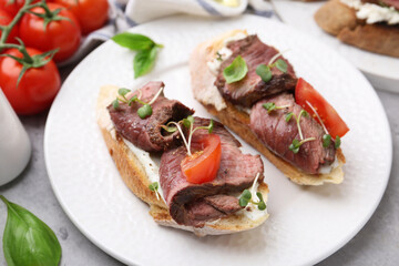 Delicious bruschettas with roast beef served on light table, closeup
