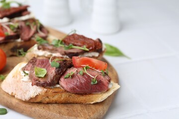 Delicious bruschettas with roast beef served on white table, closeup. Space for text