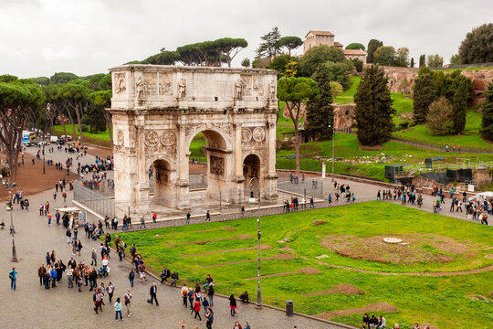 Rome, Italy - 04 November 2012: View of the majestic Arch of Constantine, standing proudly amidst a vibrant green park, bustling with people under a cloudy sky.