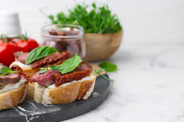 Bruschettas with roast beef, cream cheese, basil, sun-dried tomatoes and fresh vegetables on white marble table, closeup. Space for text
