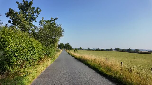 Slow motion footage driving and traveling down a country road in North Yorkshire in the UK showing British farmers fields on either side of the country lane on a sunny day in the summer time