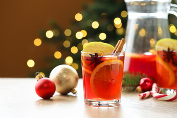 Tasty punch drink in glasses, jug and Christmas decor on wooden table against brown background with blurred lights, closeup. Bokeh effect