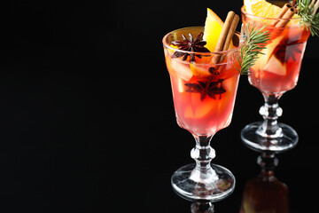 Tasty punch drink with spices in glasses on mirror surface against black background, closeup. Space for text
