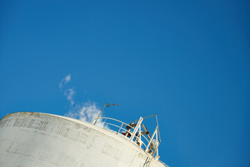 Industrial tank emitting steam against blue sky