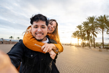 Young gen z couple enjoying piggyback ride taking selfie