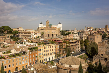 View of ancient rooftops and buildings basking in warm sunlight, with the iconic Victor Emmanuel II Monument standing tall against a blue sky, Rome, Lazio, Italy.