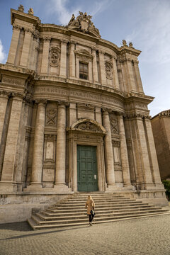 View of the grand curves and detailed carvings of the church facade rise above the steps with a lone figure, framed by the Roman sky, Rome, Lazio, Italy.