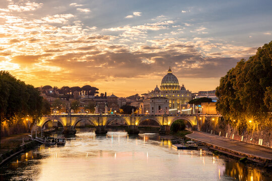 View of the Tiber River reflecting the golden sunset light illuminating the iconic St. Peter's Basilica and Ponte Sant'Angelo, Rome, Lazio, Italy.