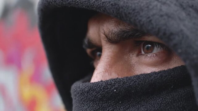 A person wearing a black hood gazes at vibrant street art in an urban environment. The close-up captures the intensity and depth in their eyes as they reflect.