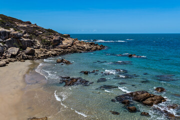 An aerial view of Rose Bay in Bowen, Queensland, reveals a stunning tropical coastline with turquoise waters, golden sand, and rocky headlands. The scene highlights coastal beauty and vibrant color.