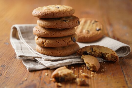 A stack of delicious chocolate chip cookies on a rustic wooden table, with some cookies broken and crumbs scattered around