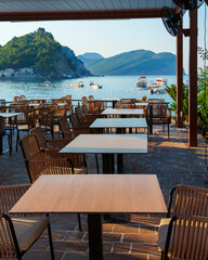 cozy outdoor cafe or restaurant located on embankment with panoramic view of Petrovac city, Montenegro, tables and chairs in front of sea and beach, beautiful nature with hills and forest