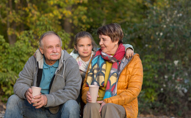 Fototapeta premium Little child girl hugs grandpa and grandmother On Walk iin nature on a sunny autumn day. Concept of friendly family. 