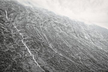 Watercourses on steep mountainside under dramatic sky in black and white