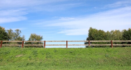 Wooden post fence at the top of a grassy hill. Blue sky and trees on behind. Bottom view. Background for copy space.