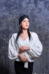 In a dark room stands a beautiful girl with long hair, dressed in a black leather skirt and a white blouse. Her outfit is designed in a business style. This is the image of a business woman.