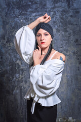 In a dark room stands a beautiful girl with long hair, dressed in a black leather skirt and a white blouse. Her outfit is designed in a business style. This is the image of a business woman.