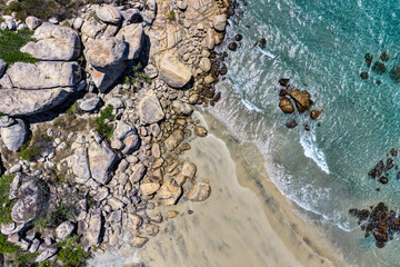 An aerial view of Rose Bay in Bowen, Queensland, reveals a stunning tropical coastline with turquoise waters, golden sand, and rocky headlands. The scene highlights coastal beauty and vibrant color.
