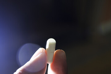 Person carefully holds single white pill between two fingers. Close up representing medicine,...