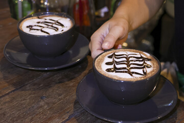 Barista serving delicious cup of warm cappuccino with chocolate art on rustic wooden table. An inviting and cozy beverage for relaxing moment at coffee shop
