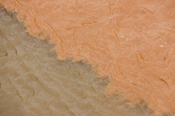 Natural abstract background shows powerful confluence of two rivers. muddy brown water mixes with sediment creating turbulent pattern and texture from an aerial view