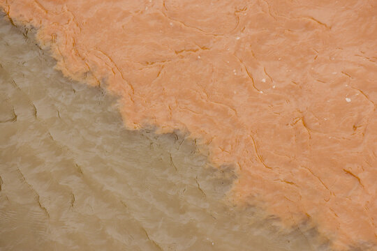 Natural abstract background shows powerful confluence of two rivers. muddy brown water mixes with sediment creating turbulent pattern and texture from an aerial view