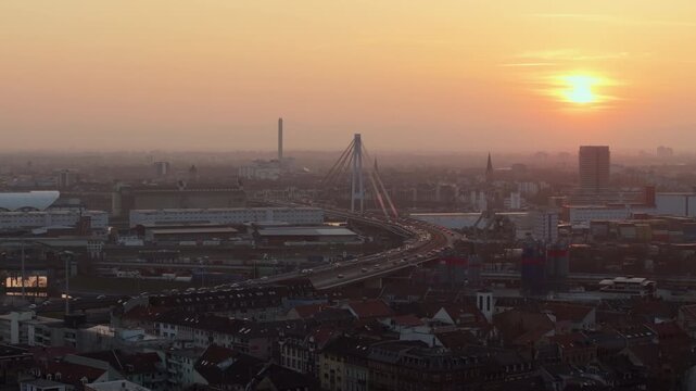 Golden hour sunset over german city of Mannheim. Aerial view showing city rooftops, Kurt Schumacher Brucke bridge, and heavy car traffic