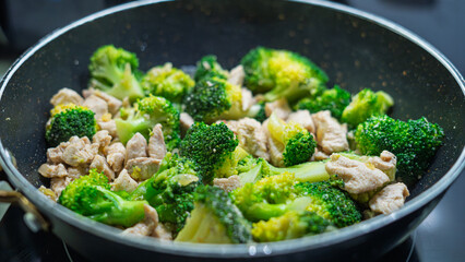 Ground meat and broccoli stir-frying in a non-stick pan. Mixed vegetables and protein cooking together on stovetop. Healthy homemade meal preparation concept with overhead view.