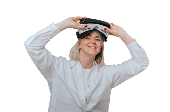 Blonde short haired Scandinavian girl in white shirt using vr googles smiles wide sitting on transparent background. Relaxed caucasian short haired woman enjoys virtual reality headset