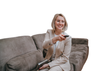 Blonde young American woman in beige suit sitting on transparent background holds remote control, switching channels on tv. Smiley successful businesswoman relaxing home after work