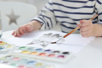 Little boy with brush drawing cat at white table indoors, closeup