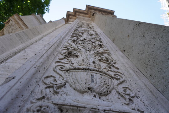 Detailed stone architectural carving on a historical building fa&ccedil;ade, captured from a low angle. Ornamental floral patterns and classical design elements emphasize heritage craftsmanship and cultural 