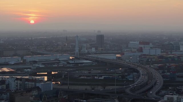 High angle view of Mannheim, Germany, during hazy sunset. Cars drive on highway and bridges over Neckar river on a misty evening