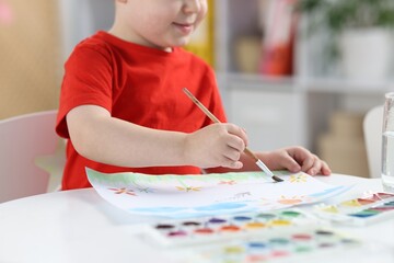 Little boy with brush drawing at white table indoors, closeup