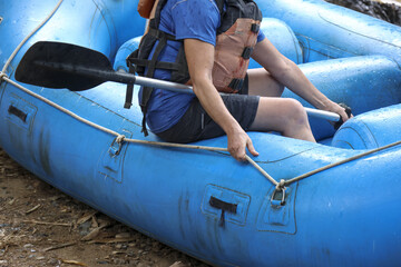 Active person holding paddle in blue inflatable raft, preparing for an exciting water sport adventure on river. This outdoor activity thrilling summer journey