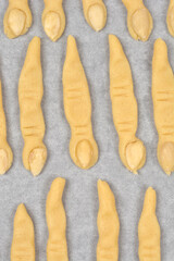 An overhead shot of numerous unbaked sugar cookies shaped like creepy witch fingers with almond fingernails, laid out on a baking tray lined with parchment paper