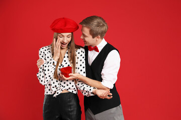 Man surprising his girlfriend with gift on red background. Romantic present