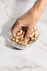 Female hand grabbing pistachio nuts from a bowl on kitchen countertop surface