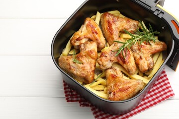 Grilled chicken wings with french fries and rosemary in air fryer basket on white wooden table, closeup. Space for text