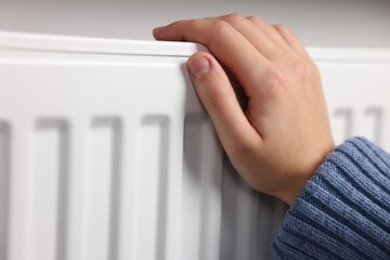 Woman warming her hand near radiator indoors, closeup. Space for text