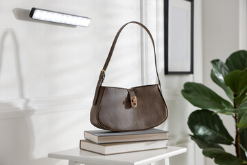 Stylish LED lamp on white wall, stool with books and bag indoors