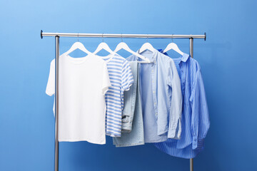 Different stylish clothes hanging on rack near blue wall indoors