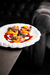 seared meat with a dark sauce, garnished with bright yellow edible flowers and red berries, against a dark, minimalist background.