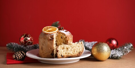 Christmas food. Delicious Panettone cake and festive decor on beige table against red background